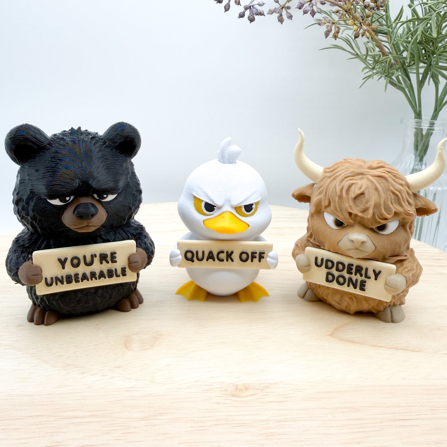 Three animal figurines holding signs with humorous text on a wooden surface.