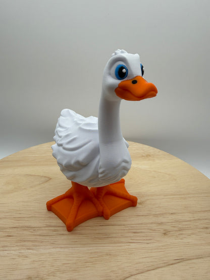 White 3D printed goose with blue eyes and orange beak and feet standing on a wooden surface
