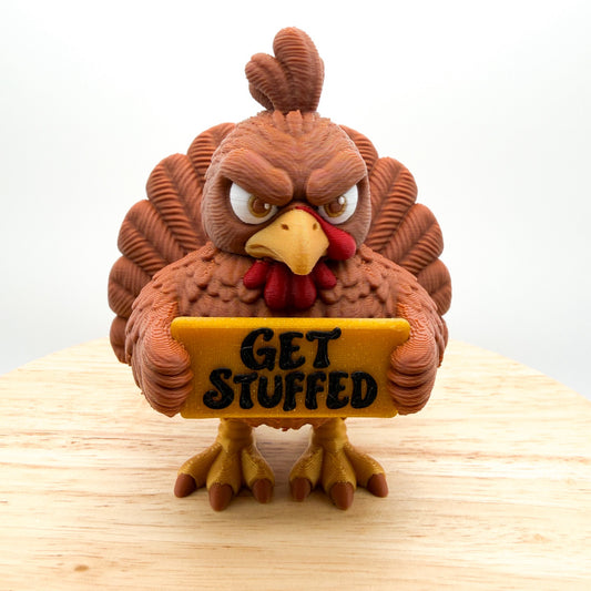 Turkey figurine with a grumpy expression and a fanned tail, holding a gold sign that says GET STUFFED, on a white background